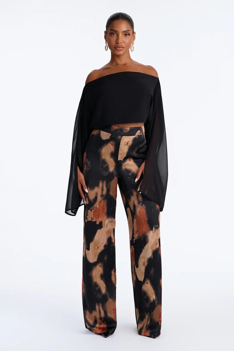 Woman wearing a black off-the-shoulder crop top with sheer sleeves and high-waisted abstract print wide-leg pants.