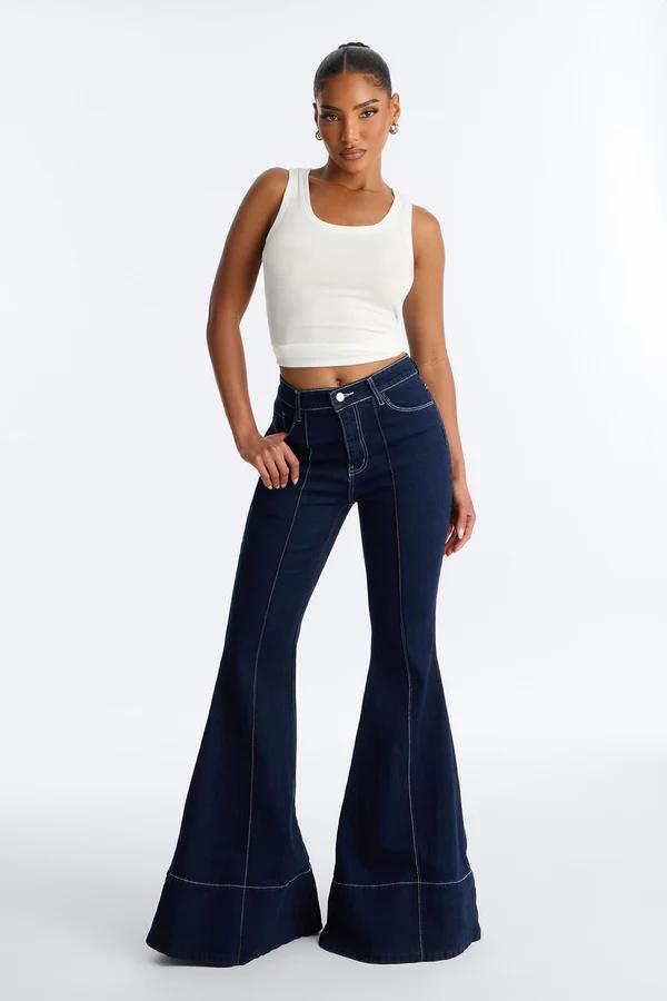 Mujer con top corto blanco acanalado y jeans acampanados azul oscuro con costuras blancas visibles, de pie de cuerpo entero.