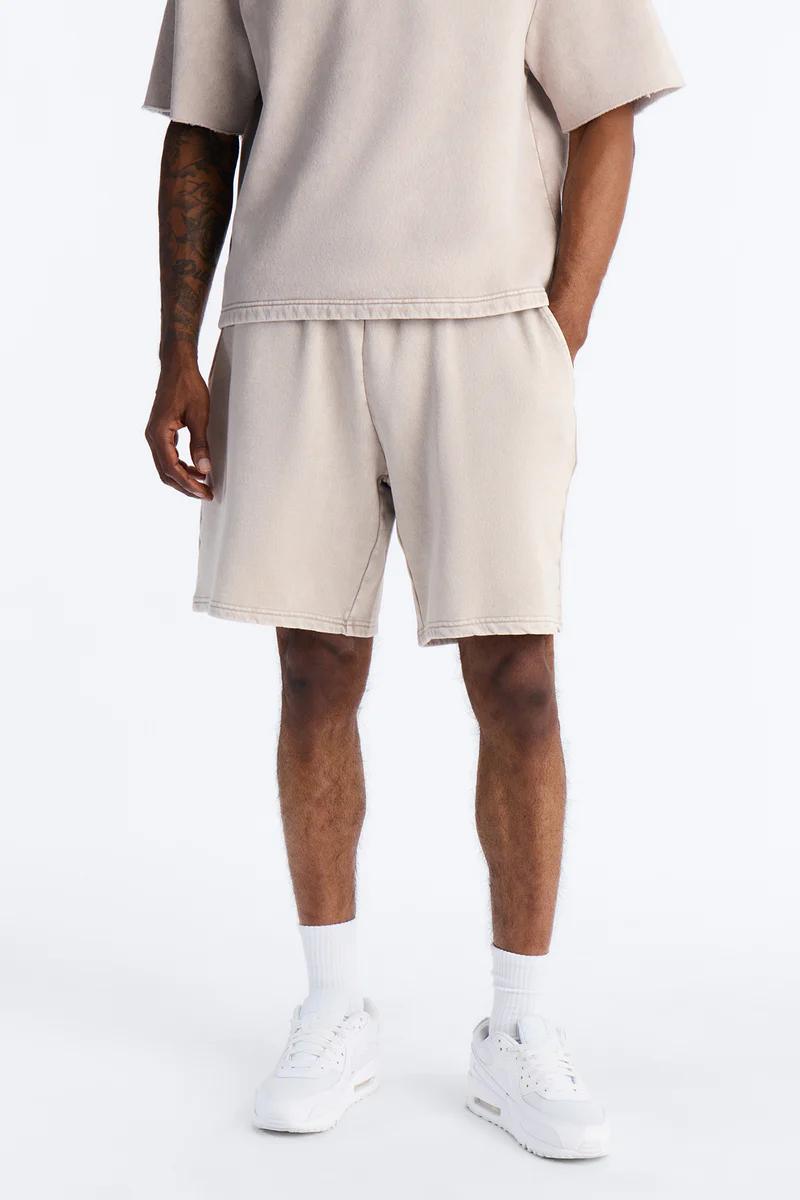 Man in a relaxed fit sand-colored t-shirt and matching drawstring shorts with white sneakers, showcasing comfortable men's loungewear.