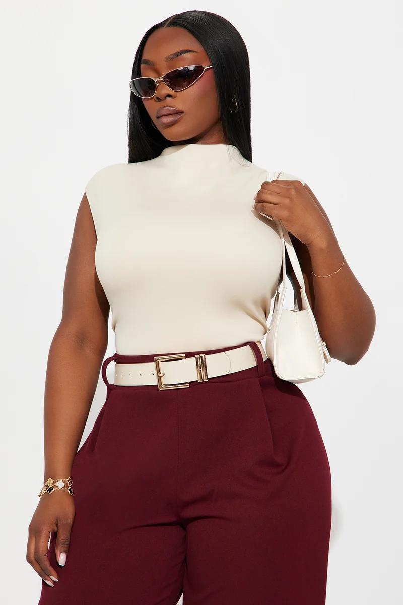 Plus size woman wearing a sleeveless cream mock neck top and burgundy high-waisted trousers.