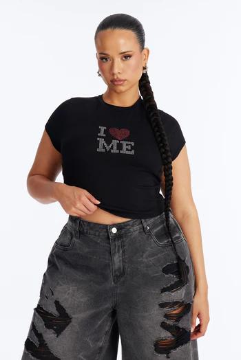 Woman wearing a black crop top with sparkly 'I ❤️ ME' text, paired with distressed dark grey wide-leg jeans. Long braided ponytail.