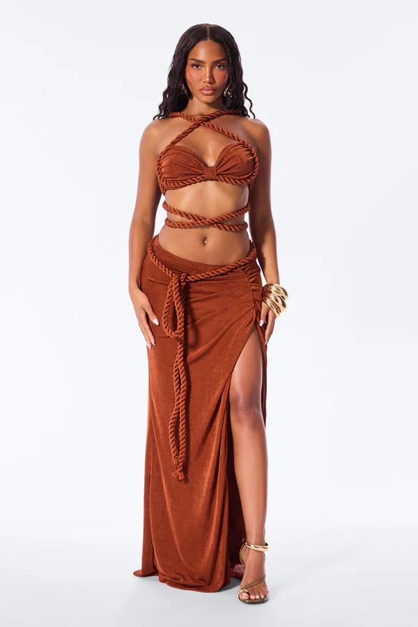 Woman wears a beige crochet strapless crop top with gold ring and a matching open-knit maxi skirt with ruffles.