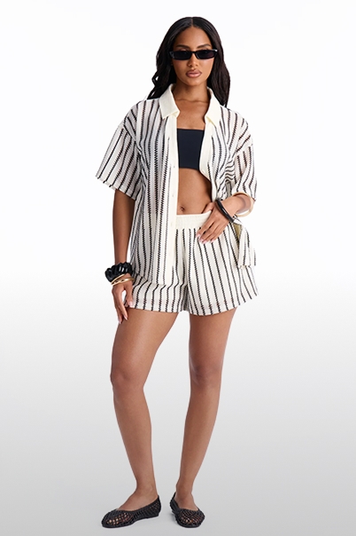 Modelo con elegante conjunto de camisa manga corta y shorts a rayas crema y negras, con bandeau. Nueva colección resort.