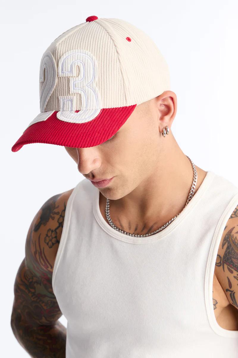 Stylish corduroy baseball cap in beige and red with '23' design, worn by a person in a white tank. Highlighting trending men's headwear.
