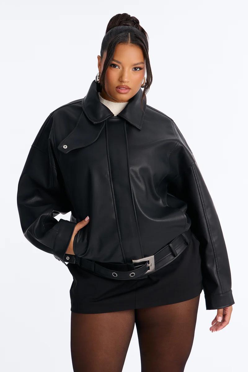Plus size model wearing an oversized black faux leather jacket and belted mini skirt.