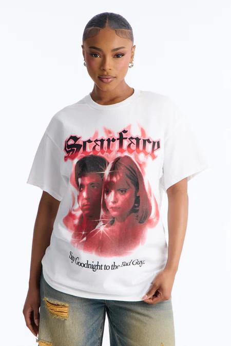 Mujer con camiseta blanca de Scarface con Al Pacino y Michelle Pfeiffer en rojo, rodeados de llamas. Con vaqueros desgastados, mira al frente.