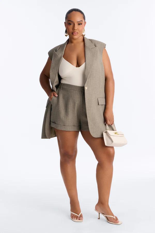 Stylish woman wears a taupe pinstripe sleeveless blazer and tailored shorts matching set with an off-white bodysuit. Shop new spring fashion.