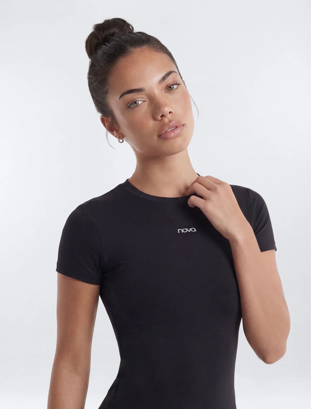 Woman wearing a black Nova brand activewear t-shirt with a high bun against a white background, showcasing fitted women's athletic apparel.