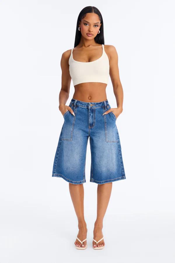 Woman in cream ribbed crop top, faded blue wide-leg denim culottes with large pockets, and light flip-flops on white.
