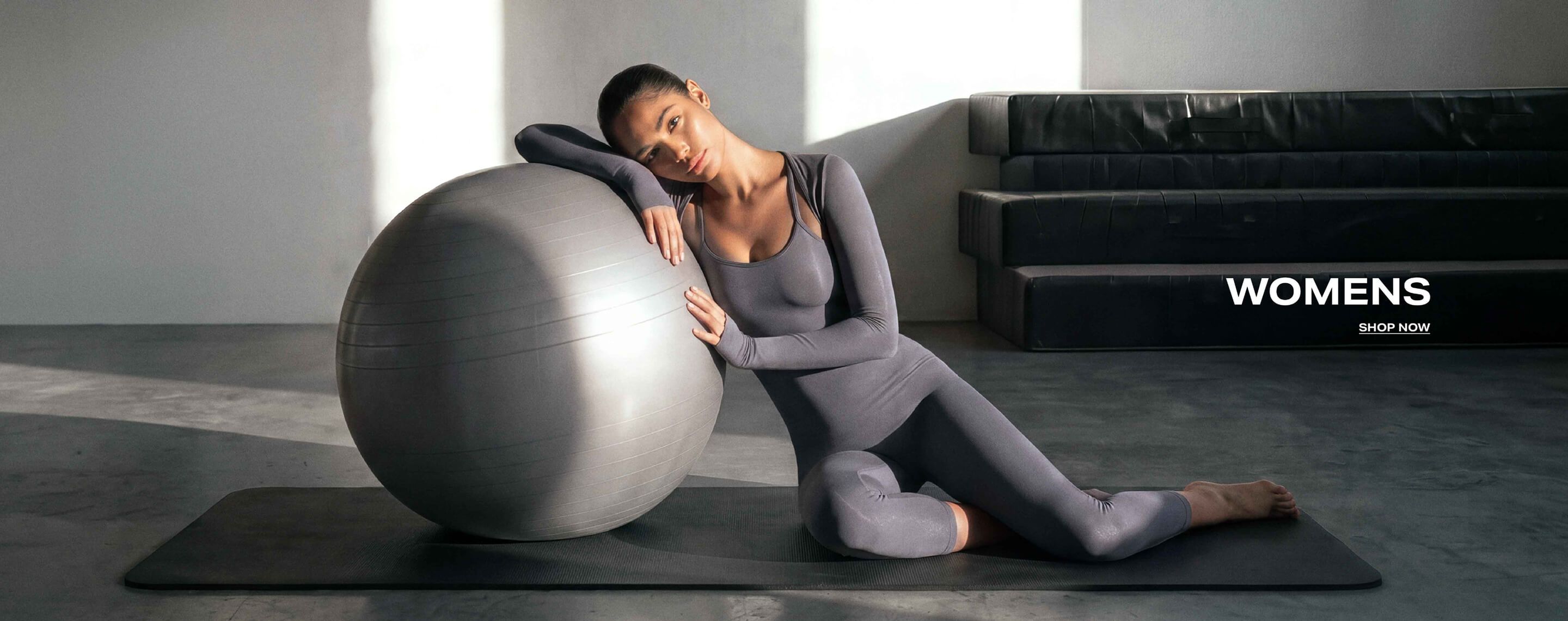Woman in a grey activewear set leans on a fitness ball, promoting the womens athletic clothing collection with a Shop Now link.