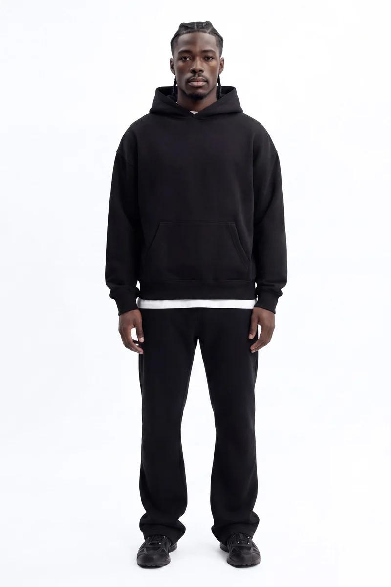 Man in a relaxed black oversized hoodie and black sweatpants, showcasing comfortable men's casual loungewear against a white background.