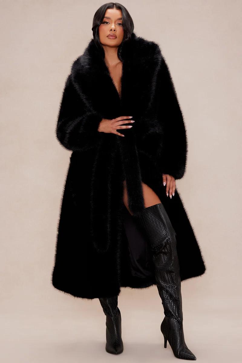 Woman posing in a luxury long black faux fur coat and textured thigh-high boots, showcasing the new winter outerwear fashion collection.