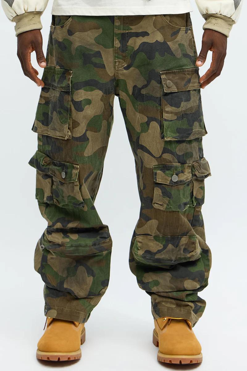 Pantalones cargo camuflados en una persona con botas color canela. Muestra bolsillos utilitarios, presentando la colección de streetwear masculina.