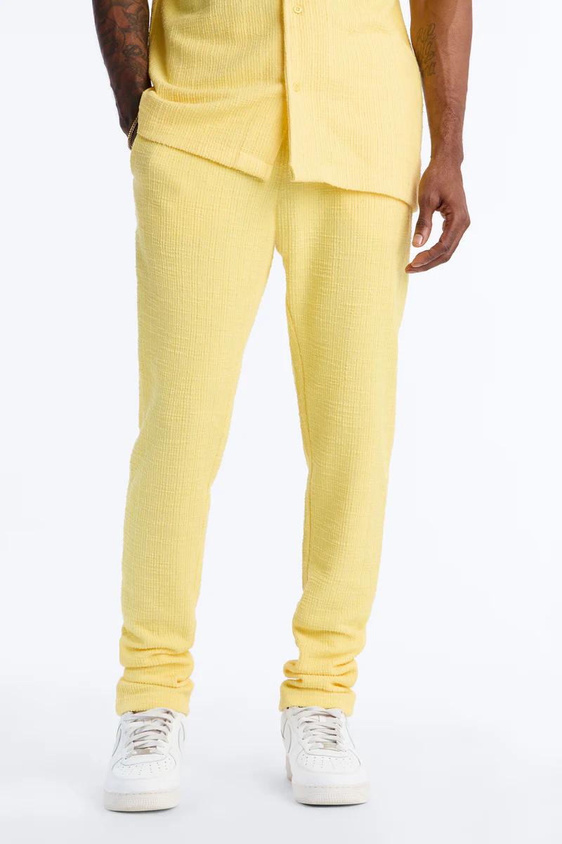 Pantalones texturizados amarillos brillantes y camisa a juego en un hombre, con zapatillas blancas. Destaca un look de moda casual masculino y elegante.