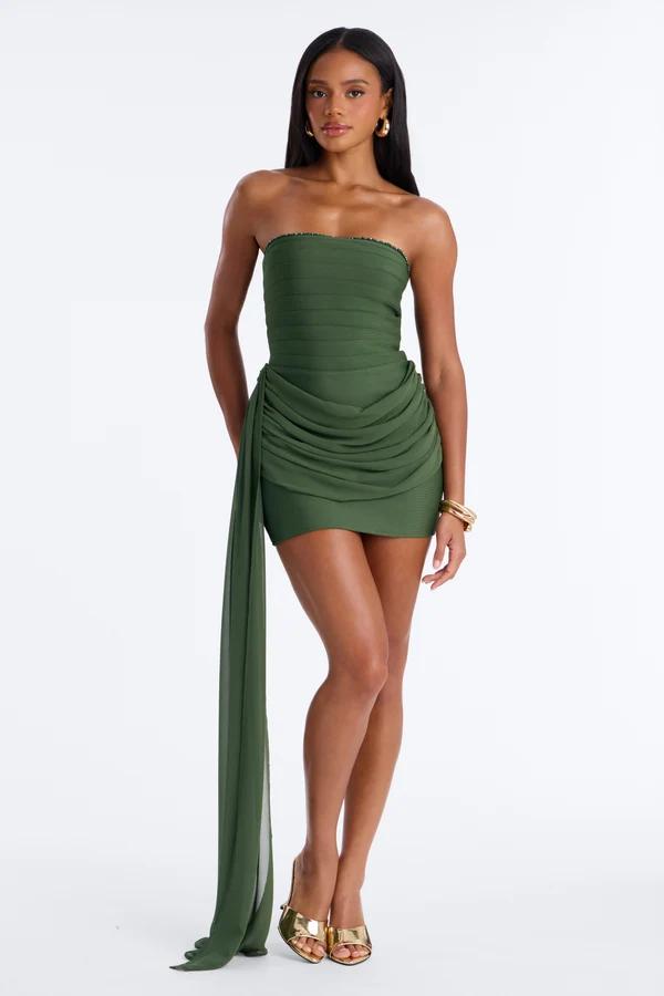 Woman posing in an olive green strapless mini dress with a draped side sash and gold heels, highlighting elegant party cocktail attire.
