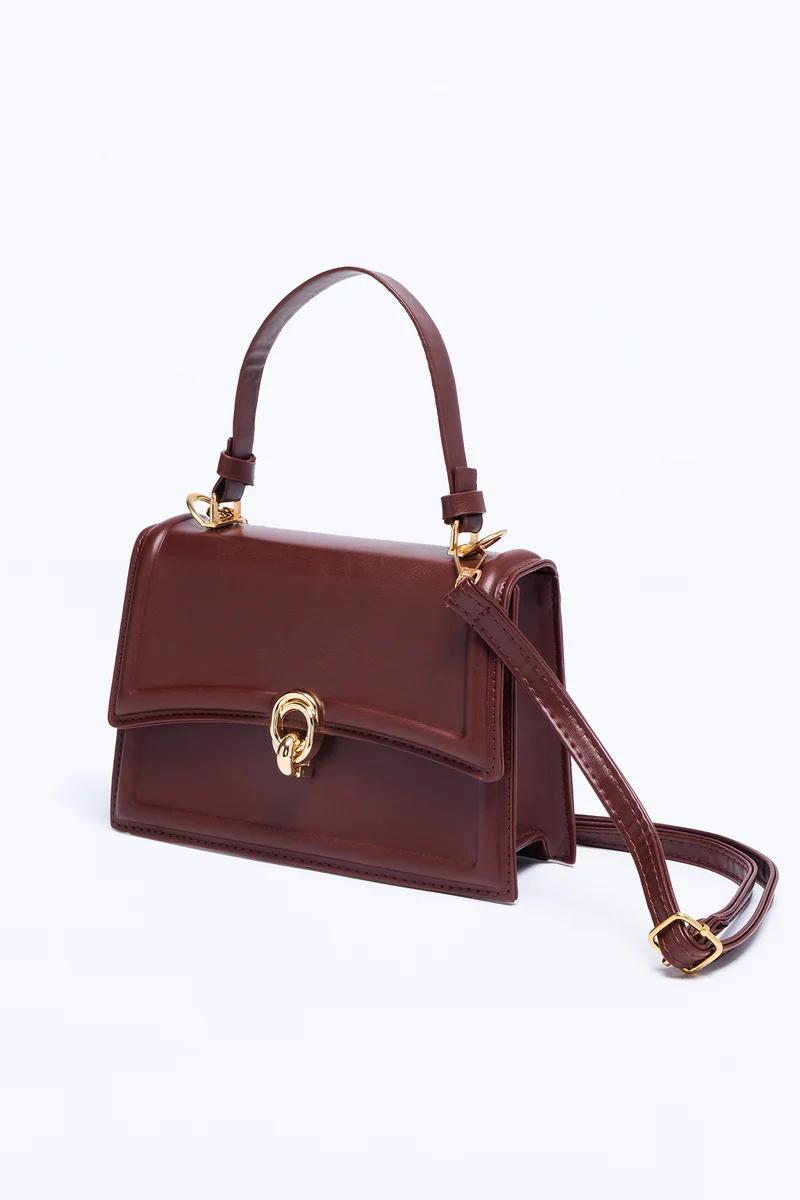 Elegante bolso de piel burdeos con asa superior, correa bandolera ajustable y broche dorado metálico.