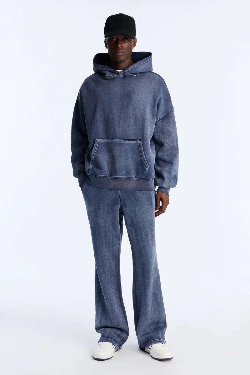 Stylish man models a faded blue oversized hoodie and matching sweatpants loungewear set, complete with black cap and white sneakers. Shop the look.