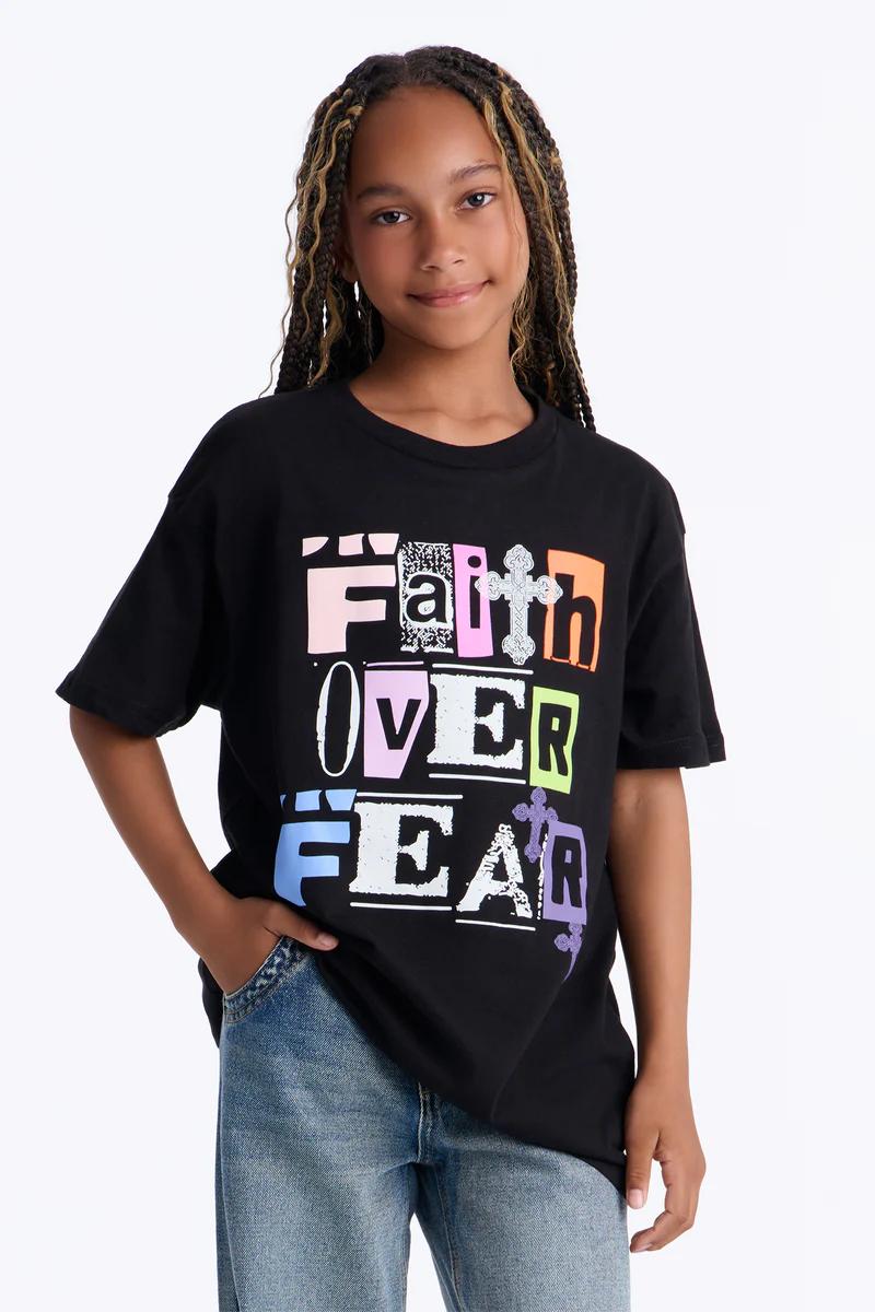 Girl models black 'Faith Over Fear' graphic t-shirt & jeans. Youth apparel, children's fashion statement tee.