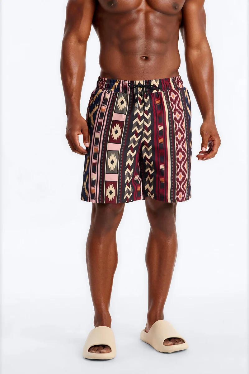 Man modeling vibrant patterned men's shorts in various colors with beige slides, perfect for stylish summer and beachwear.