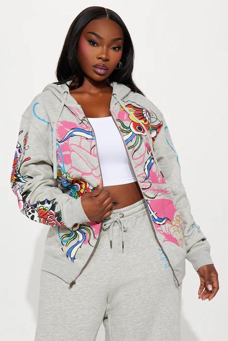 Person wearing a grey zip-up hoodie featuring vibrant pink, red, blue tattoo-style graphics, white crop top, and matching sweatpants.