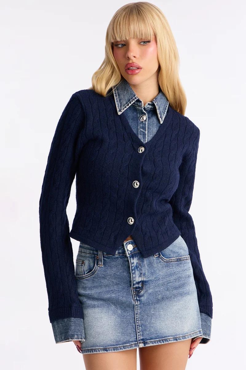 Woman wearing a cropped navy blue cable knit cardigan, denim shirt, and denim miniskirt.