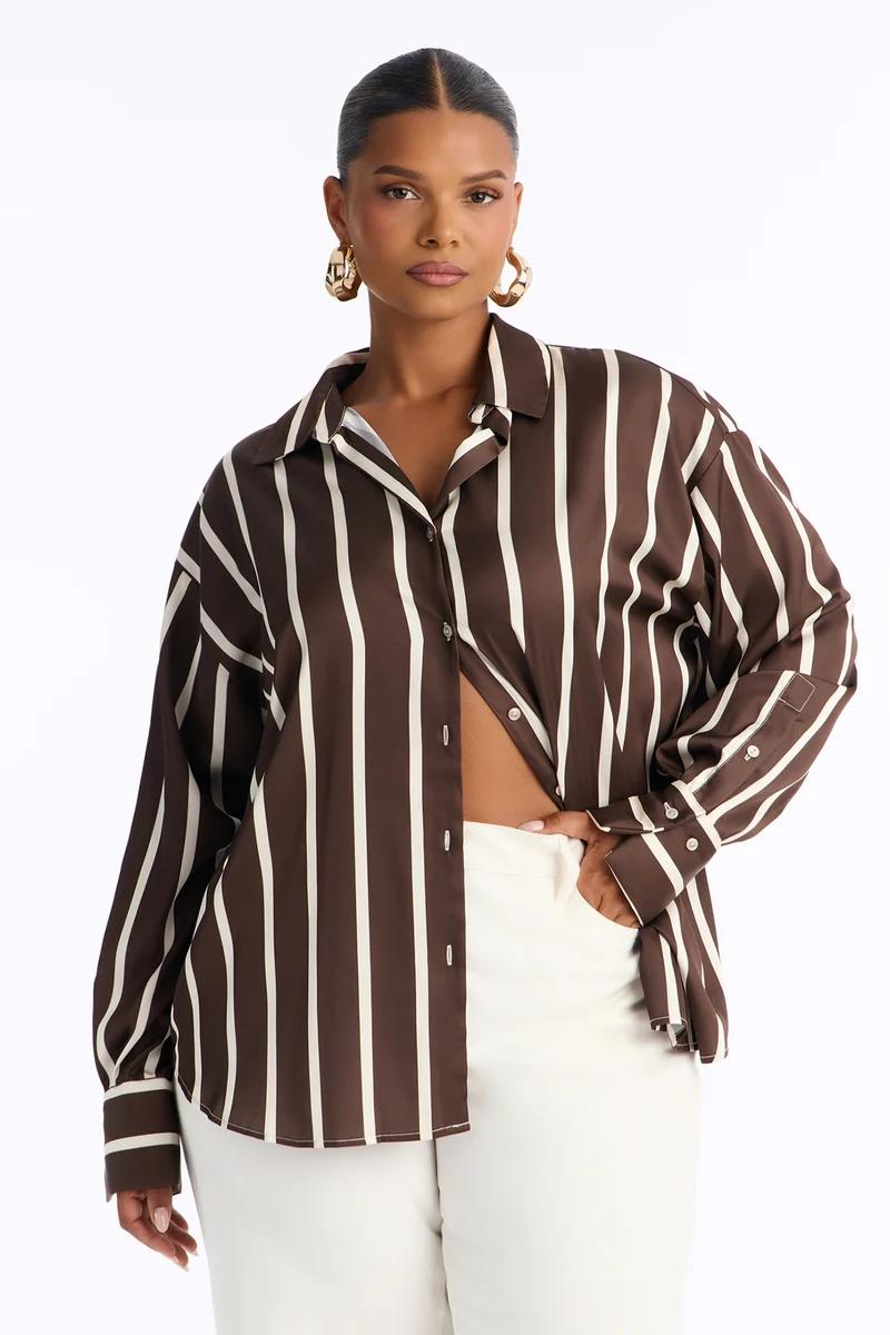 Woman in oversized brown and white striped satin shirt and white pants.