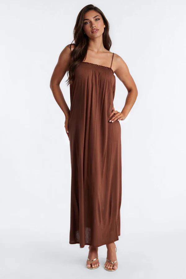 Woman wearing a stylish brown and beige striped strapless maxi dress with a clutch, highlighting elegant summer fashion.