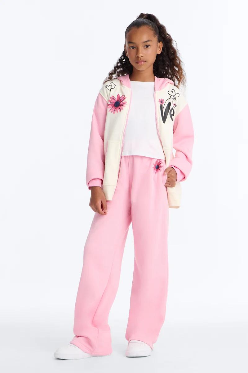 Young girl wearing a pink and cream floral zip-up hoodie and matching pink sweatpants.