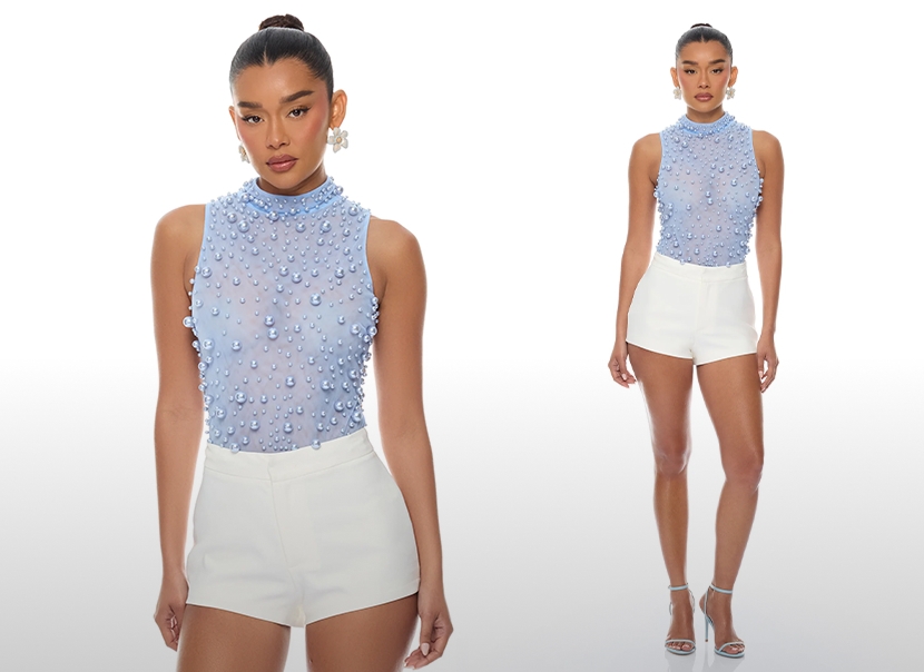 Modelo con top azul claro de cuello alto con perlas y shorts blancos, presentando una nueva colección chic. Vista cercana y completa.