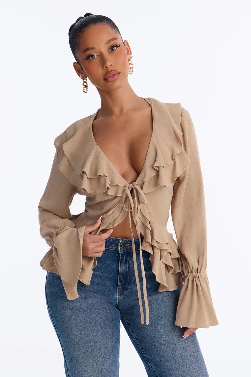 Mujer con blusa beige de volantes, lazo delantero y jeans azules.
