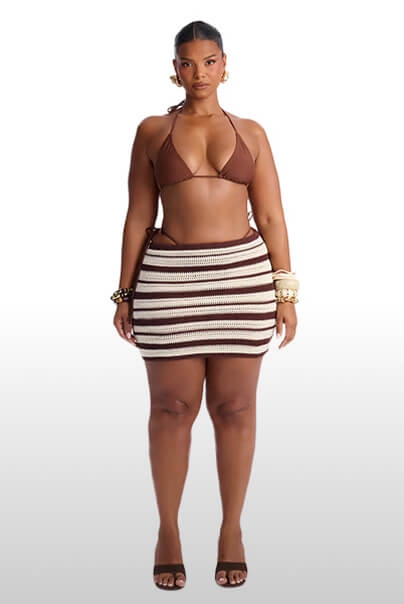 Woman models a brown halter bikini top and a cream-and-brown striped crochet mini skirt, ideal for stylish beachwear and resort fashion.