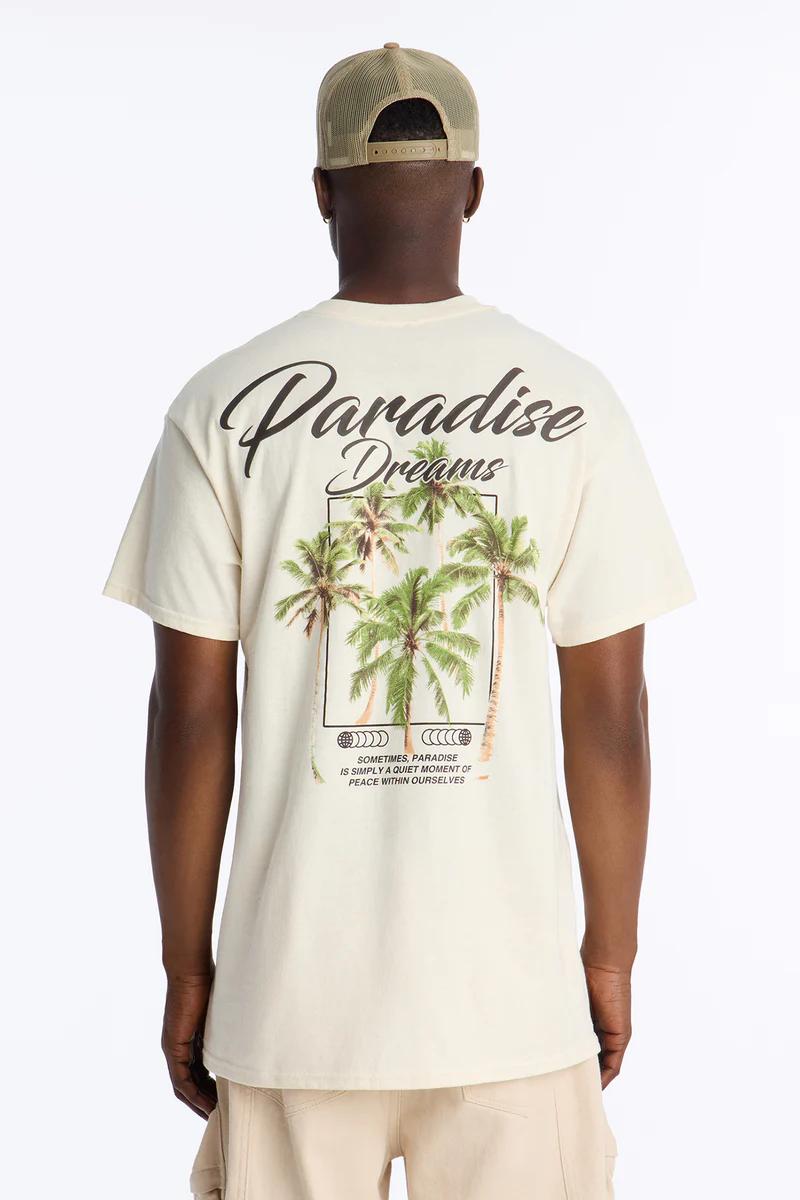 Back of man in a cream graphic tee featuring "Paradise Dreams" text and palm trees. Promotes a relaxed summer casual collection.