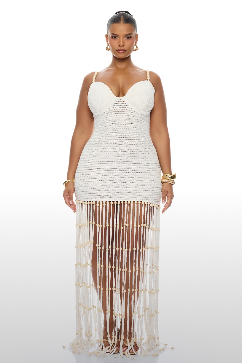 Model in a white crochet mini dress with plunging neckline, beaded fringe, gold accessories, showcasing summer resort wear.
