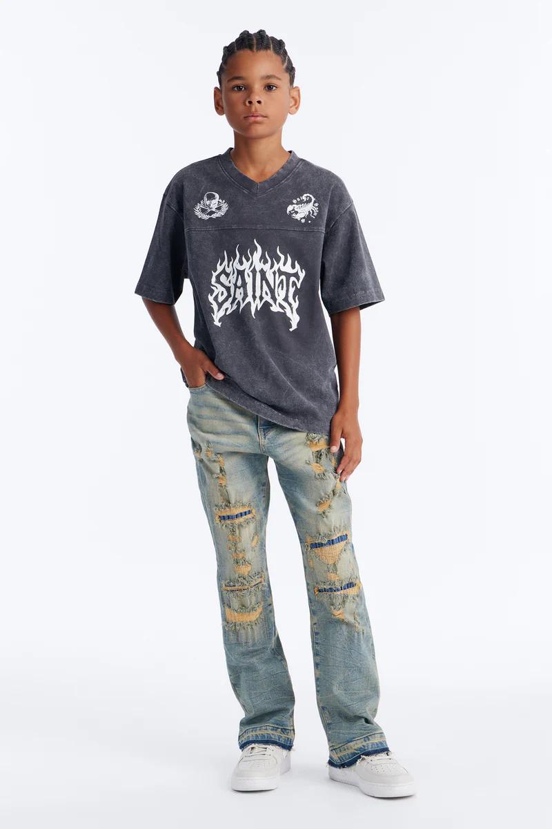 Niño con camiseta gris "SAINT" gráfica, jeans azules rotos, zapatillas blancas. Moda urbana juvenil casual.