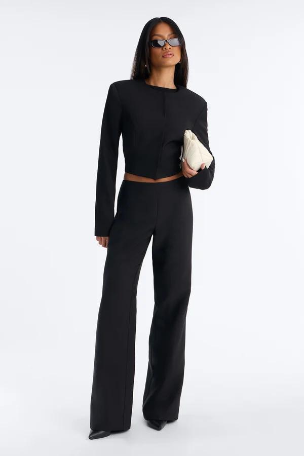 Mujer posando con un elegante traje negro de chaqueta corta y pantalones anchos, llevando un bolso blanco. Nueva colección de moda femenina.