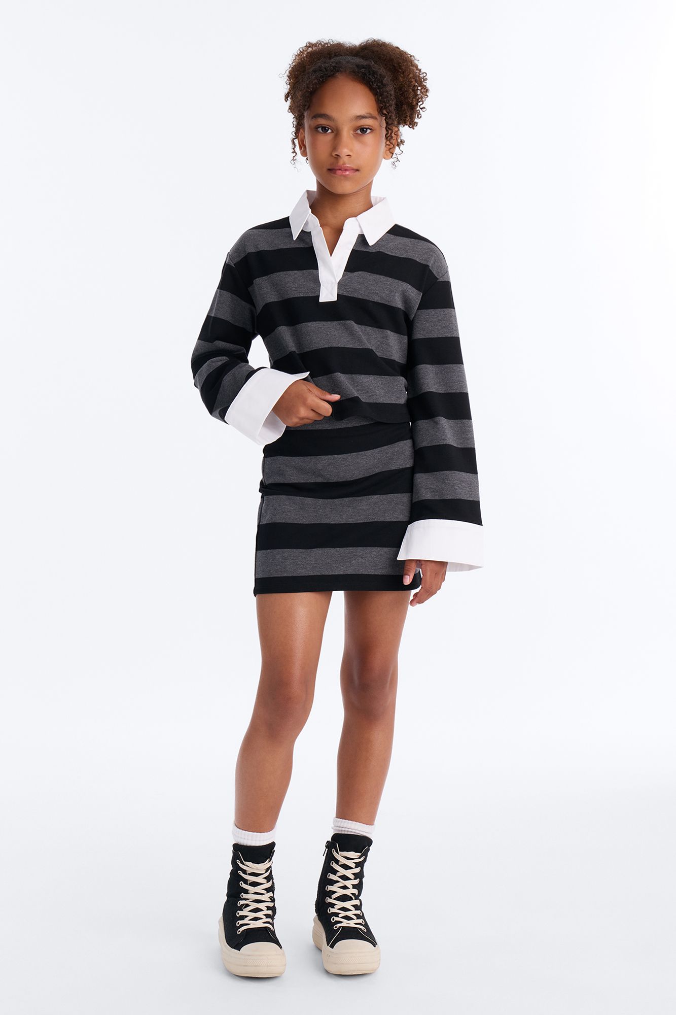 Girl in black/grey striped rugby polo & matching mini skirt, prominent white collar/cuffs, black platform sneakers.