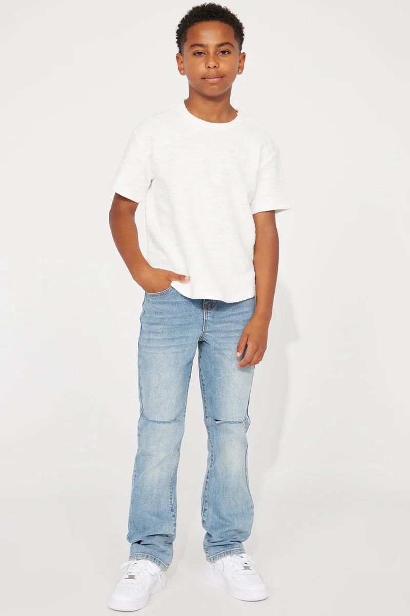Young boy in white textured t-shirt, light wash ripped jeans, and white sneakers. Casual kids outfit.