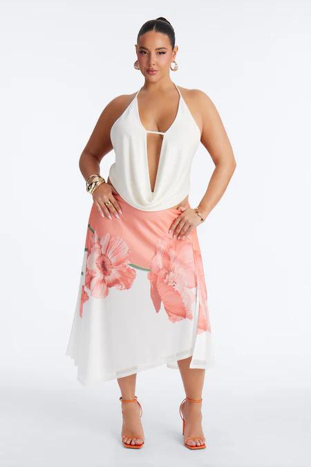 Woman in white cowl neck halter top, white midi skirt with coral floral print, gold jewelry, and orange heels.