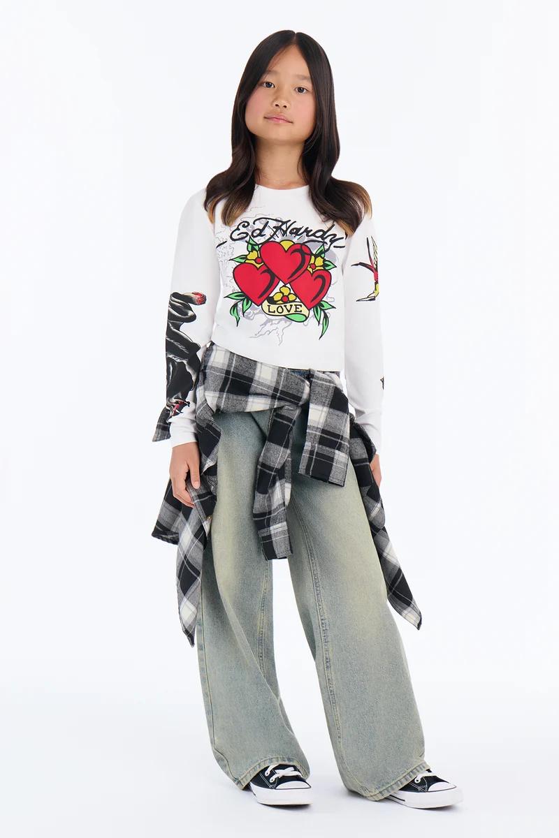 Niña con camiseta de manga larga Ed Hardy, vaqueros anchos y camisa de cuadros en la cintura.