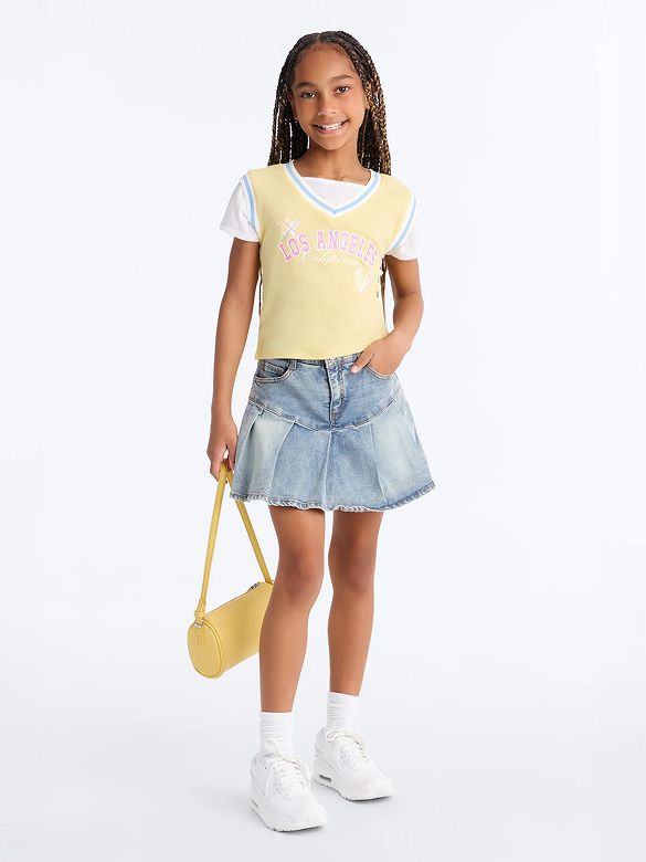 Smiling girl wears a yellow Los Angeles top, pleated denim skirt, white sneakers, and matching yellow bag, showcasing trendy girls' summer fashion.