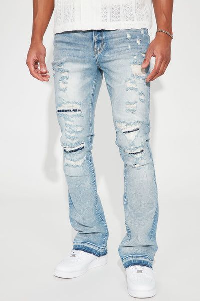 Light wash distressed denim jeans for men, featuring rips and a relaxed fit, paired with white sneakers and a textured white top. Shop casual streetwear.