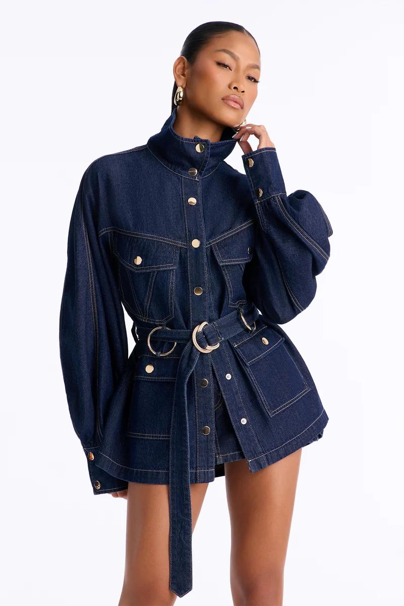 Woman in a belted dark wash denim jacket with puff sleeves and gold buttons.