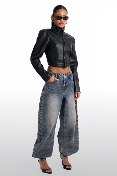 Modelo con una chaqueta corta de cuero sintético burdeos y pantalones anchos gris oscuro para la nueva colección de moda de otoño.