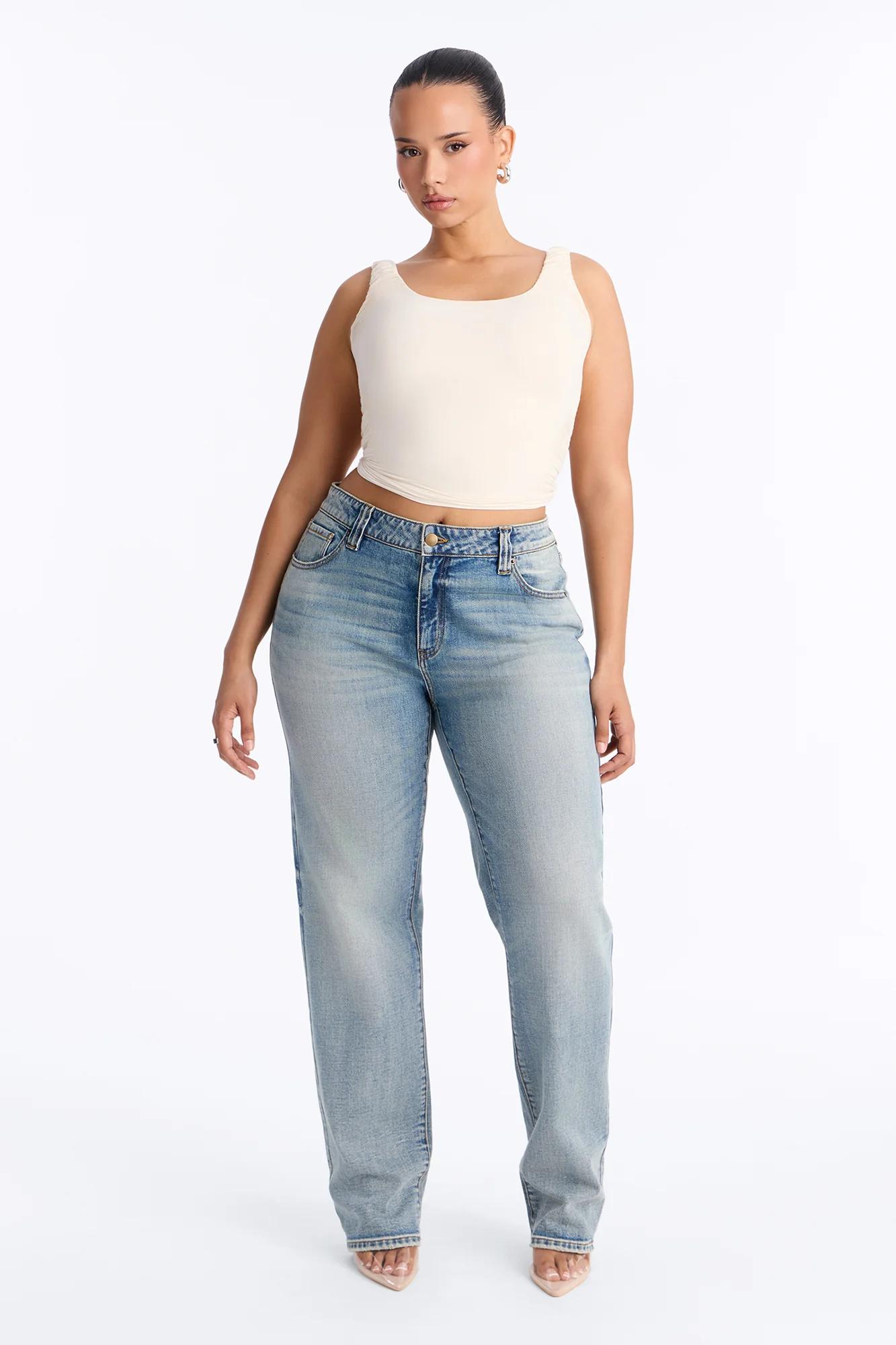 Mujer con top corto crema sin mangas y jeans rectos de lavado claro de la nueva colección de denim femenino sobre fondo blanco.