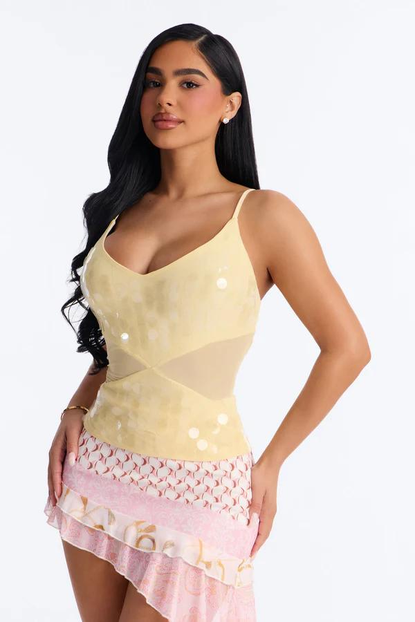 Mujer con camisola amarillo pálido de lentejuelas y malla, y minifalda escalonada rosa, blanca y dorada, posando sobre fondo blanco.