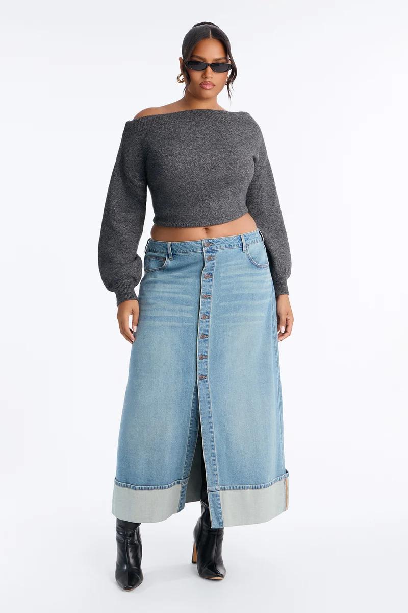 Modelo de talla grande con suéter gris corto de hombros caídos y falda larga de mezclilla con botones. Look ideal de moda otoñal.