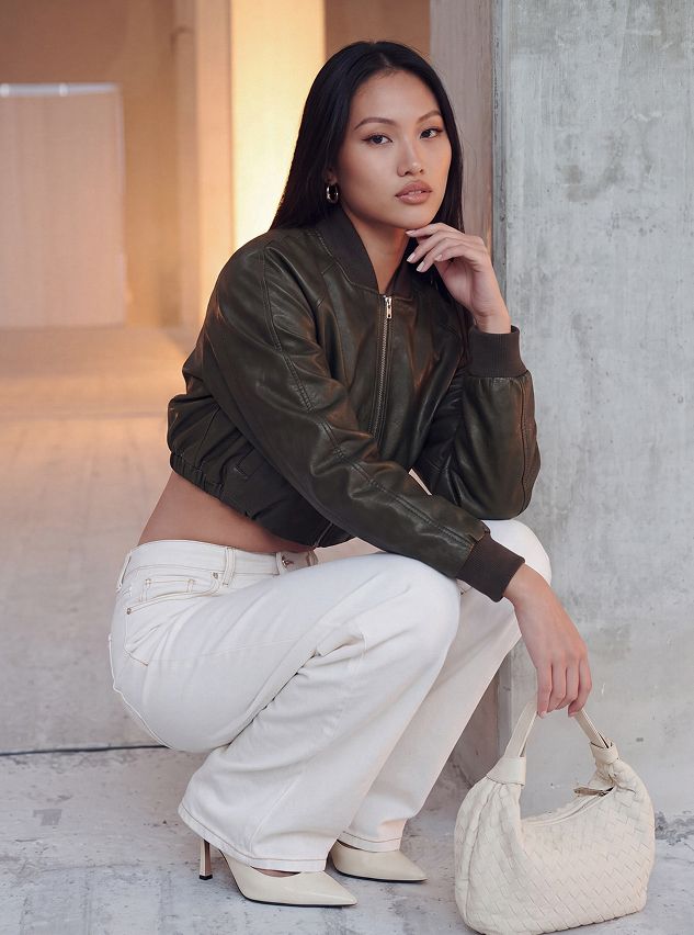 Woman wearing a green cropped bomber jacket and white wide-leg jeans, showcasing trendy fall streetwear fashion from a new collection.