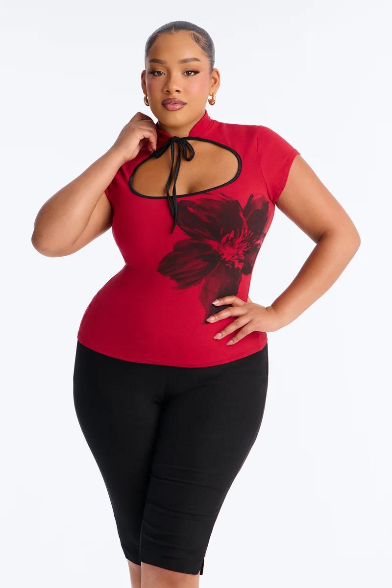 Plus size model in red keyhole top with floral print and black capri pants.