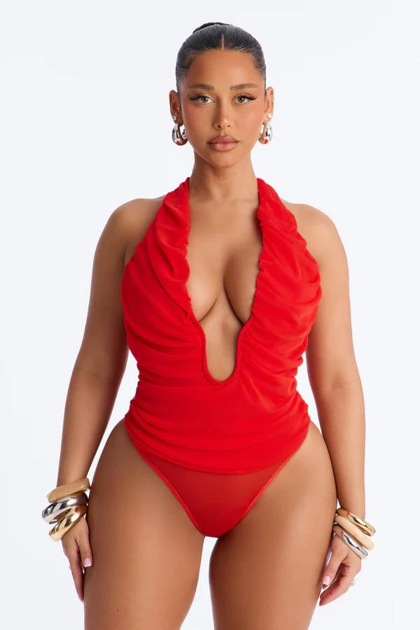 Model in a red deep V-neck ruched halter swimsuit, striking a pose against a white background. Wearing silver hoop earrings and stacked bangles.