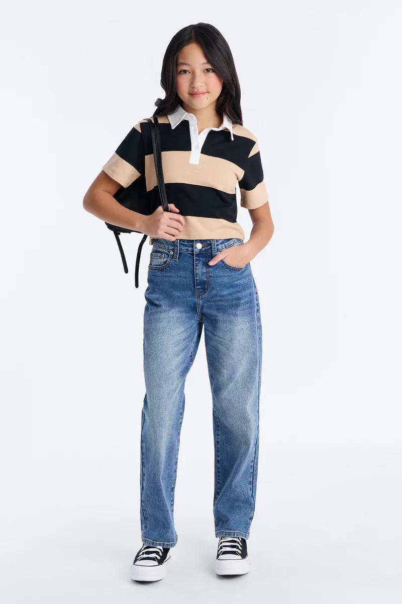 Joven con polo de rayas negras y beige, jeans anchos, zapatillas y mochila. Moda casual.